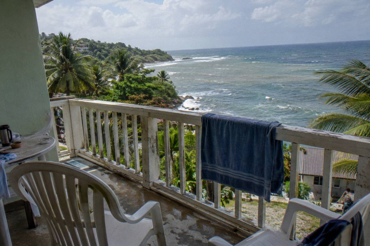 A simple guest-room balcony with two chairs overlooking tropical foliage and the sea (illustrative image, not the hotel)